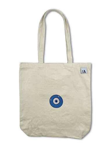 Blue Evil Eye embroidered on a beige cotton canvas tote bag with an RA Attire woven logo label. Featured on white background image. 